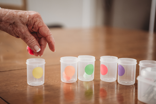 A wrinkled hand grips an object over a small cylindrical container.