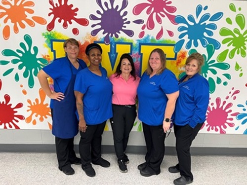 Five women pose in front of a colorful mural.