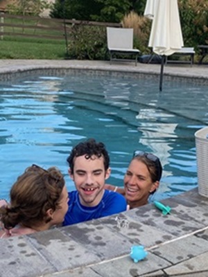 A young male client floats in a swimming pool. Two female therapists support him on either side.