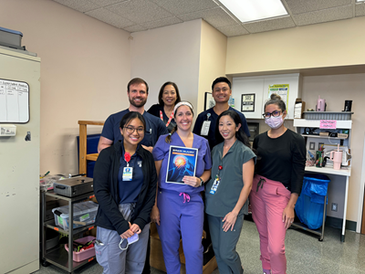 A group of hospital workers wearing scrubs. A woman in the middle holds a document with the words "Brain Injury."