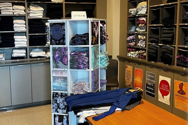 A display shelf and table with clothing. In the background, two walls of shelves are stacked with clothes. 